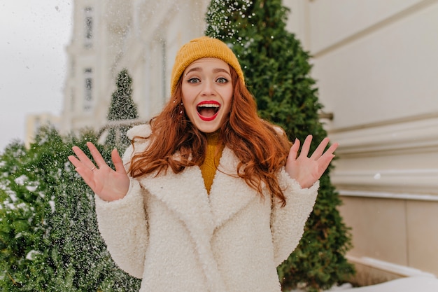 Foto grátis feliz menina de gengibre se divertindo em um dia frio de inverno. mulher ruiva emocional posando com neve.