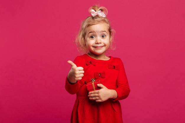 Feliz menina loira de vestido vermelho, aparecendo o polegar