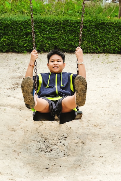 Foto grátis feliz menino de esporte asiático jogue no campo de jogos swing no garden.