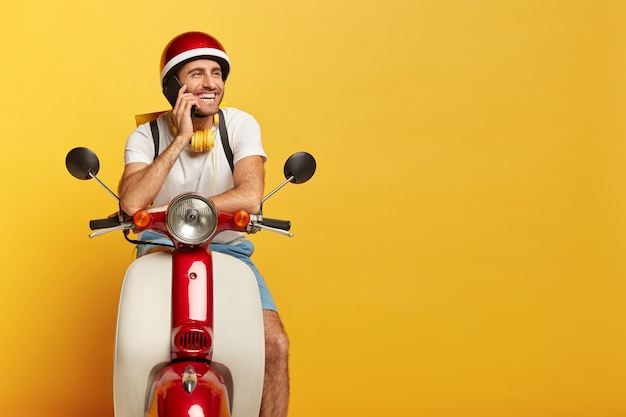 Feliz motorista masculino bonito em scooter com capacete vermelho