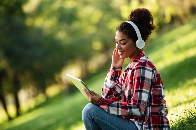 Feliz mulher africana jovem sentado ao ar livre no parque.