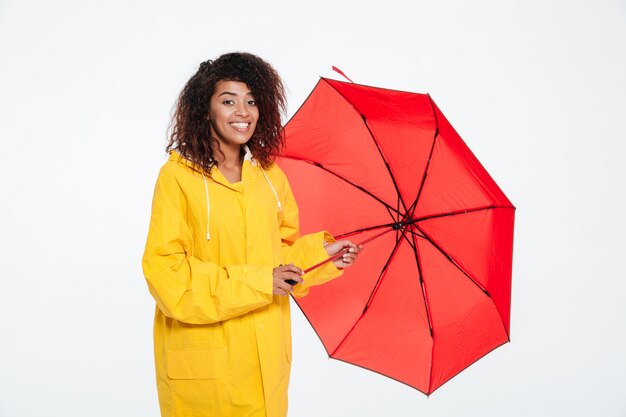 Feliz mulher africana na capa de chuva posando com guarda-chuva