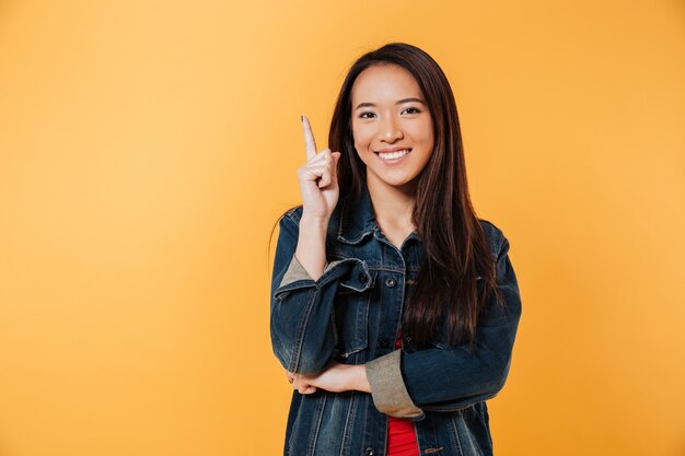 Feliz mulher asiática na jaqueta jeans apontando para cima