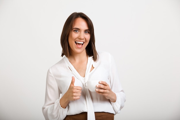 Foto grátis feliz mulher bem sucedida polegares para cima, dê aprovação, beber café