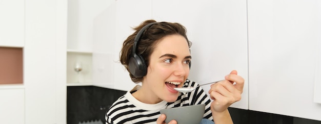 Foto grátis feliz mulher bonita comendo cereais de pequeno-almoço com leite como refeição da manhã segurando tigela e colher