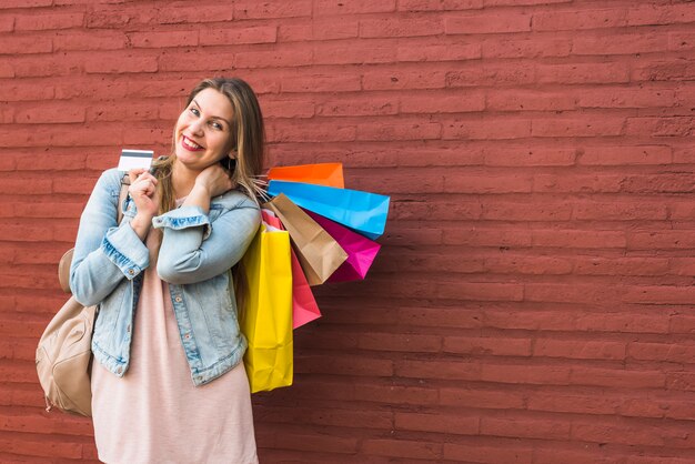 Feliz, mulher, ficar, com, bolsas para compras, e, cartão crédito, em, parede tijolo