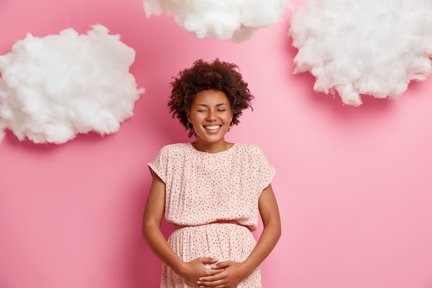 Feliz mulher grávida de pele escura toca a barriga grande, se preocupa com o futuro filho, sorridente futura mãe tem bom humor, fica de olhos fechados, antecipa se tornar mãe. Maternidade, expectativa