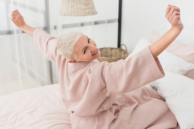 Feliz mulher idosa em roupão, estendendo-se na cama