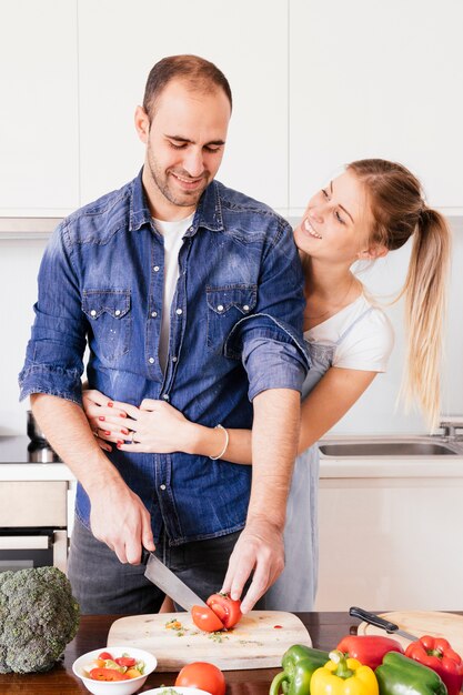 Feliz, mulher jovem, amando, dela, marido, legumes cortantes, com, faca, em, cozinha