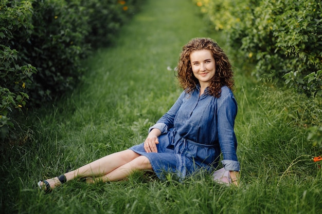 Feliz mulher jovem com cabelos cacheados castanhos, vestido, posando ao ar livre em um jardim