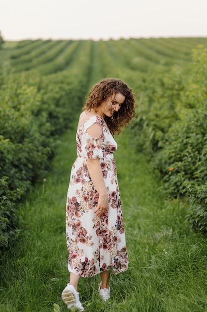 Feliz mulher jovem com cabelos cacheados castanhos, vestido, posando ao ar livre em um jardim