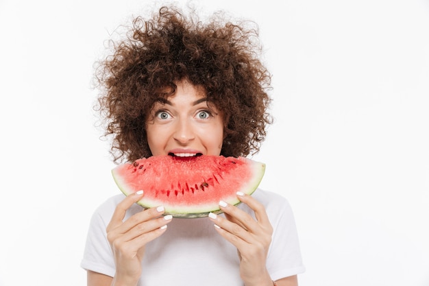 Feliz mulher jovem com cabelos cacheados, comendo melancia