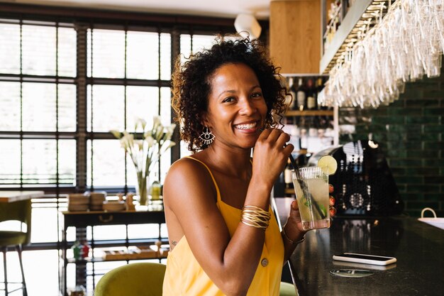 Feliz, mulher jovem, sentando, em, barra, contador, copo segurando, de, coquetel, em, a, restaurante