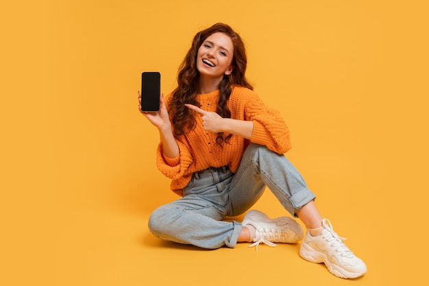 Foto grátis feliz mulher milenar mostrando a tela do smartphone e apontando para ela