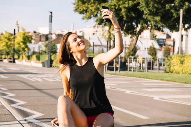 Feliz, mulher senta-se, ligado, skateboard, levando, selfie, com, cellphone