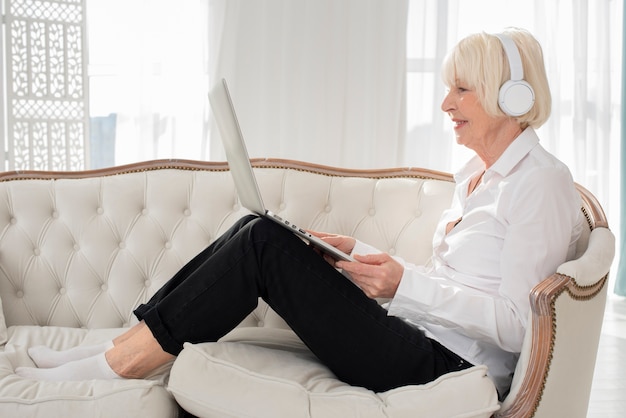 Foto grátis feliz mulher sentada no sofá com fones de ouvido e laptop