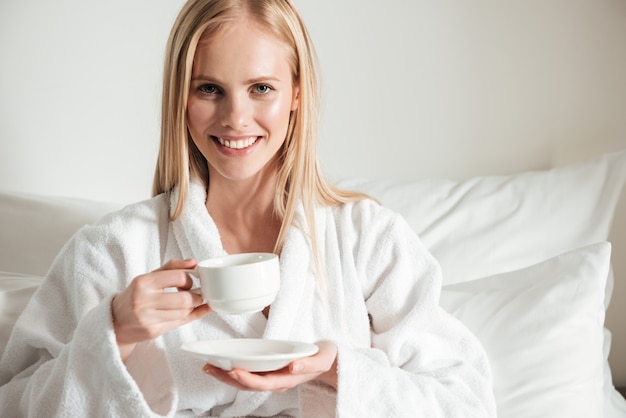 Feliz mulher sorridente em roupão segurando a xícara de café