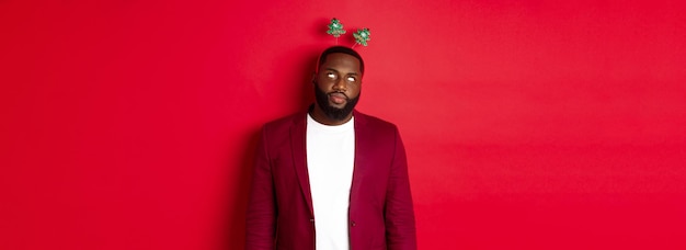 Foto grátis feliz natal homem afro-americano irritado revira os olhos usando bandana boba na festa em pé