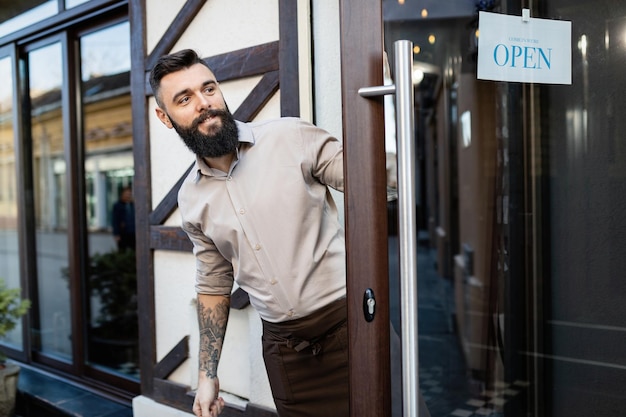 Feliz pequeno empresário parado na porta e abrindo a barra para um negócio