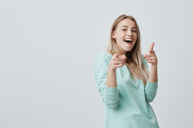 Feliz positiva alegre mulher loira com cabelos tingidos, sorrindo agradavelmente apontando com o dedo indicador para você. mulher bonita sorridente emocional com a boca aberta