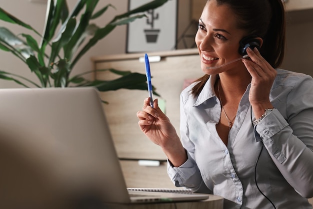 Feliz representante de atendimento ao cliente com fone de ouvido se comunicando com um cliente enquanto trabalhava no call center