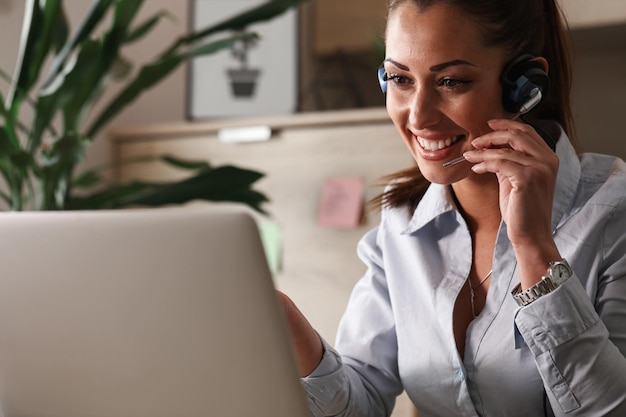 Feliz representante de atendimento ao cliente conversando com um cliente enquanto usa laptop no escritório