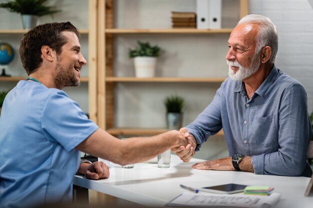 Feliz saudação médica e aperto de mão com paciente sênior em seu escritório O foco está no homem sênior