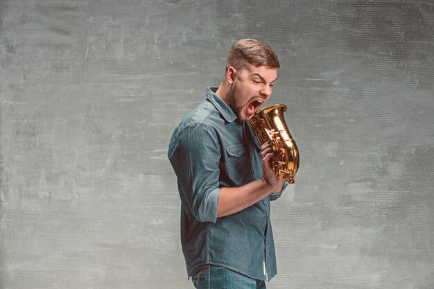 Feliz saxofonista gritando com saxofone no studio cinza