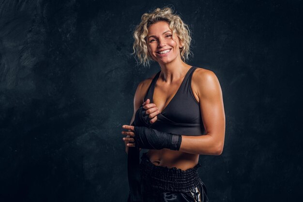 Feliz sorridente boxeador feminino está posando para fotógrafo no estúdio de fotografia escuro.