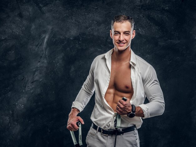 Feliz sorridente homem de camisa branca está mostrando seu pacote de seis perfeito quando abriu a camisa.