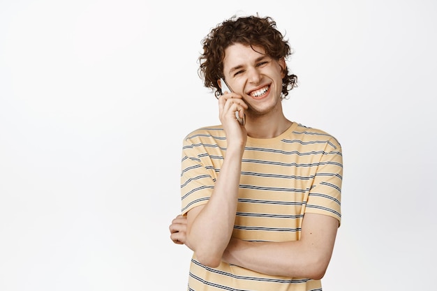 Feliz sorridente jovem falando no celular rindo de uma chamada em camiseta sobre fundo branco