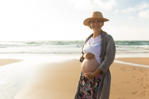 Feliz sorridente mulher grávida de mãos dadas na barriga