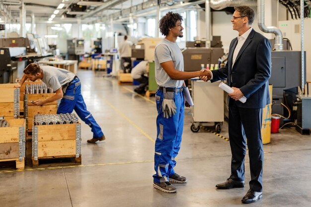 Feliz trabalhador manual negro e aperto de mão do engenheiro enquanto cumprimenta no edifício industrial