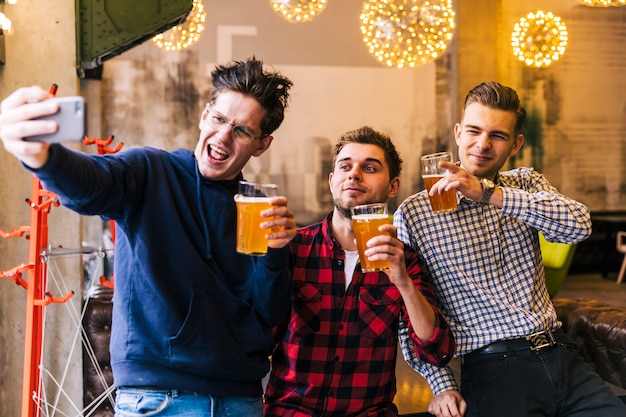 Felizes amigos tomando o selfie no celular segurando os copos de cerveja