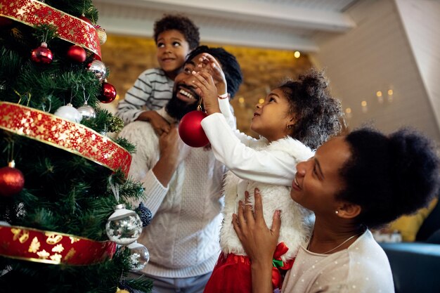 Felizes crianças afro-americanas e seus pais decorando a árvore de Natal em casa