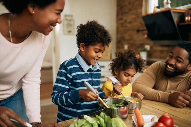 Felizes crianças afro-americanas preparando o almoço com seus pais na cozinha