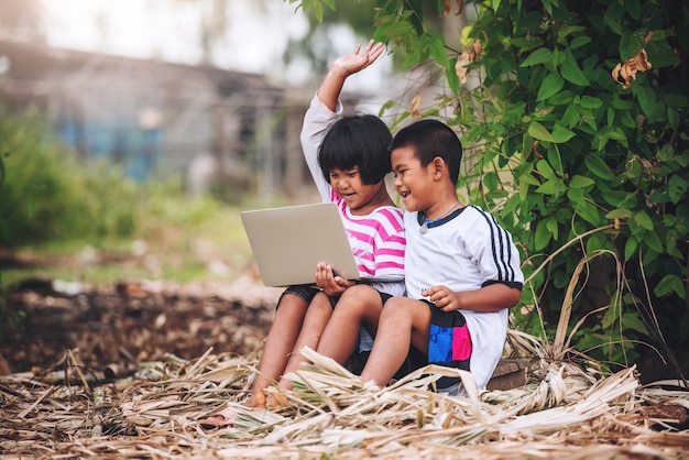 Felizes duas crianças asiáticas usando laptop para e-learning em casa escola remota no interior