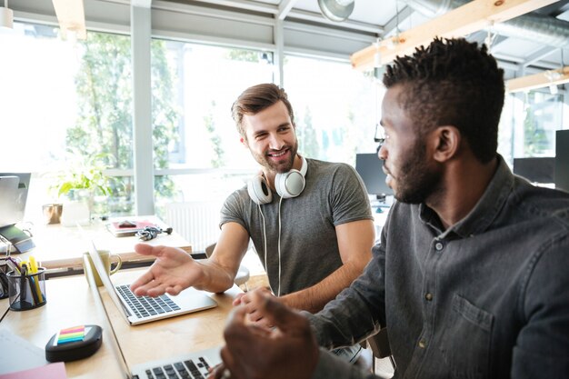 Felizes jovens colegas sentados no escritório coworking usando laptop