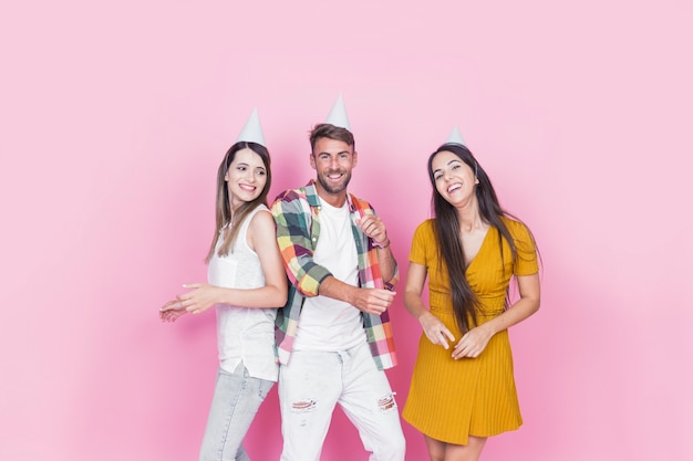 Felizes três amigos de pé contra o fundo rosa dançando juntos na festa