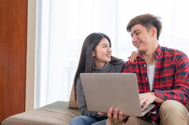 Felizmente jovem mulher bonita e homem bonito usando computador portátil no sofá no quarto em casa