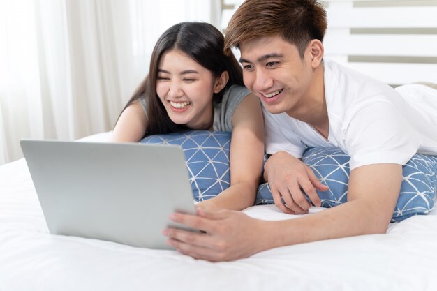 Felizmente jovem mulher bonita e homem bonito, usando o computador portátil na cama no quarto em casa