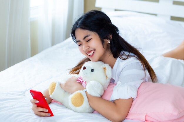 Fêmea adolescente bonita alegre com smartphone na cama