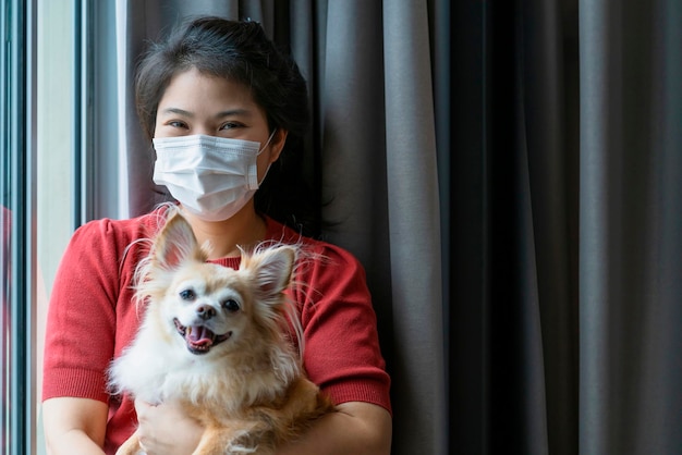 Foto grátis fêmea adulta asiática madura usando proteção de máscara facial segura cachorrinho chihuahua olhando para a câmera no isolamento do apartamento em casa fica o conceito de ordem do estado de origem
