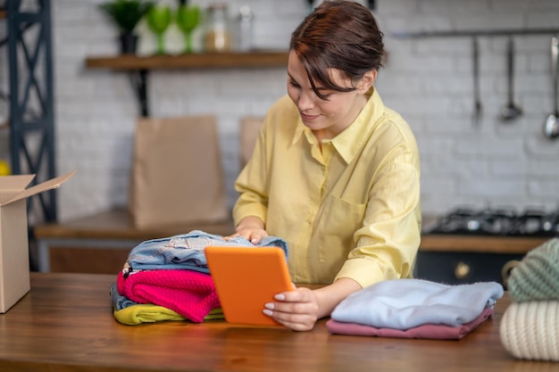 Foto grátis fêmea concentrada fotografando uma pilha de roupas coloridas na mesa usando seu computador tablet