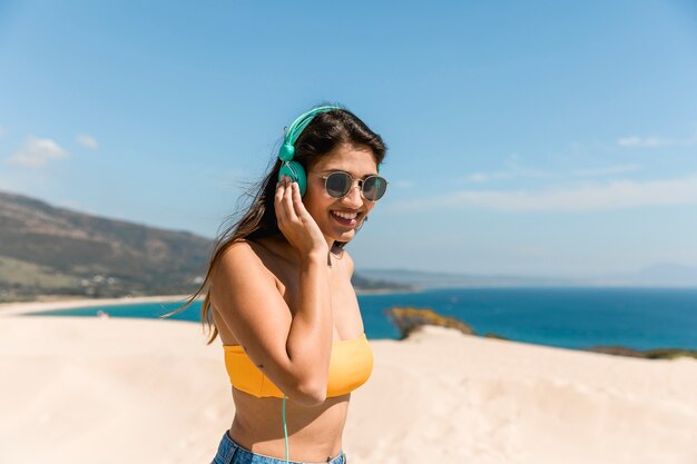 Fêmea jovem feliz ouvindo música na luz do sol na beira-mar