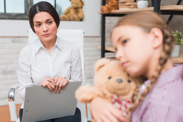 Femininas, psicólogo, com, área de transferência, e, caneta, observar, a, deprimido, menina, abraçando, dela, urso teddy