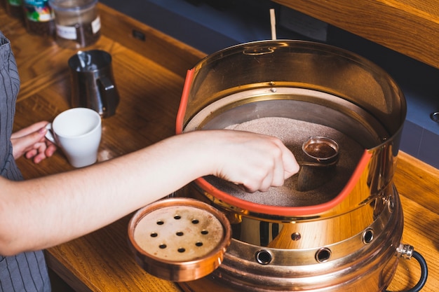 Feminino barista preparando café turco em cezve na areia no café bar