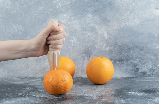 Feminino mão espremendo laranja na mesa de mármore.