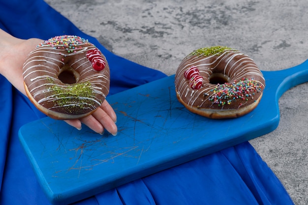 Foto grátis feminino mão segurando donut de chocolate na superfície de mármore.