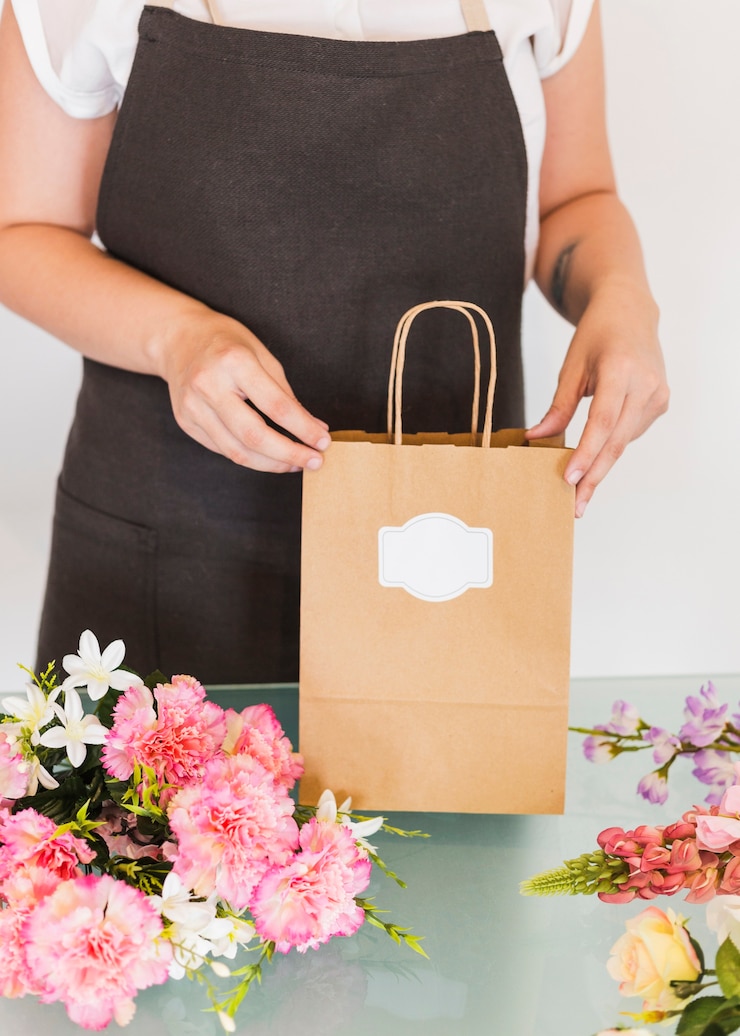 Foto grátis feminino mão segurando o saco de papel com ramo de flores na mesa